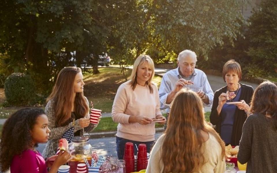 Images shows a group of neighbours eating outside. 