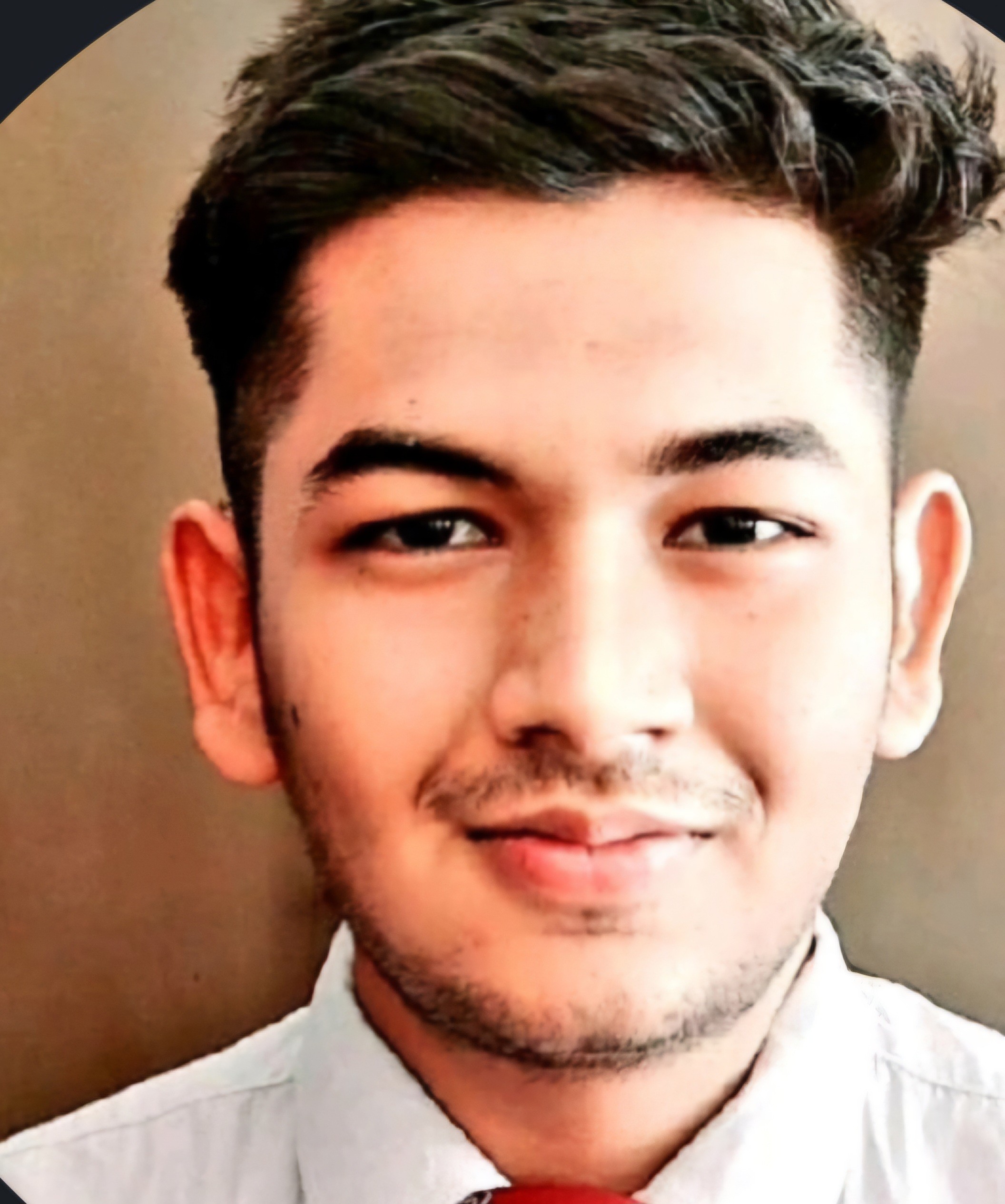 Tanveer is standing in front of a beige background, he has brown eyes and brown hair. Tanveer is wearing a white collared shirt and looking directly at the camera