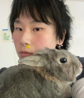 Mila has short black hair, looking at the camera, holding a small grey rabbit.