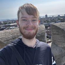 Jacob has a red hair and a beard and is smiling at the camera. 