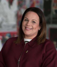 Anoushka has brown shoulder length hair, she's wearing dark red top and smiling 