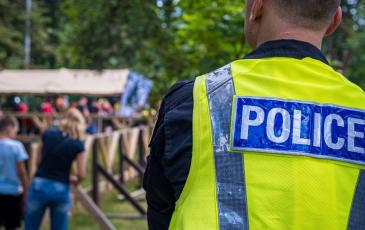 Image shows a police officer in a high-vis vest overlooking a community event