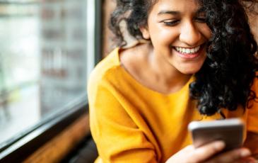 Image shows a woman looking at her phone, she looks relaxed and is smiling 