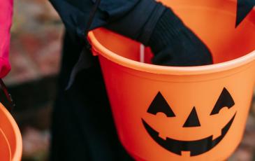 Image shows a child's hand going into a trick or treat bucket 