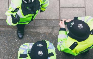 Image shows 3 police officers in a street talking, they wear high vis vests. 