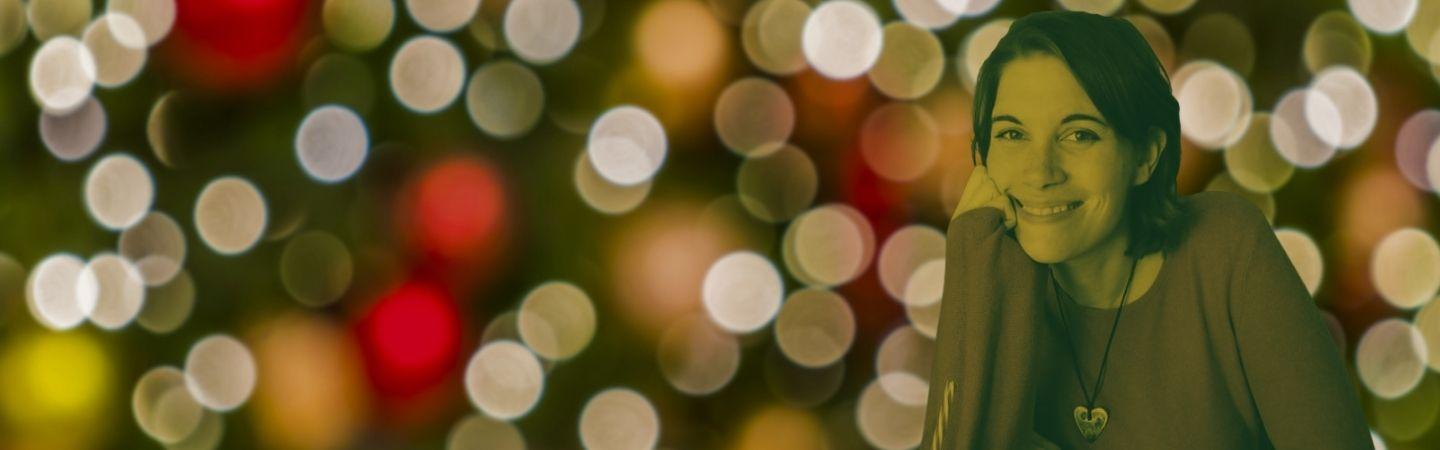 Image shows Steph against a festive tree background. She's shoulder length dark hair and she is smiling at the camera