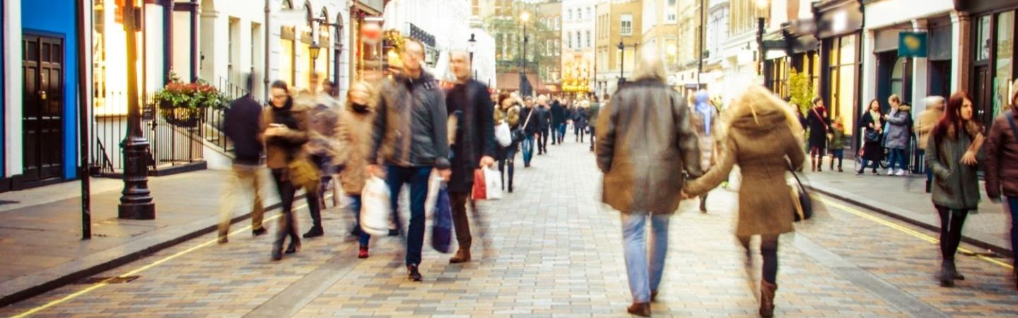 Image shows a busy pedestrianised high street, lined with shops. 