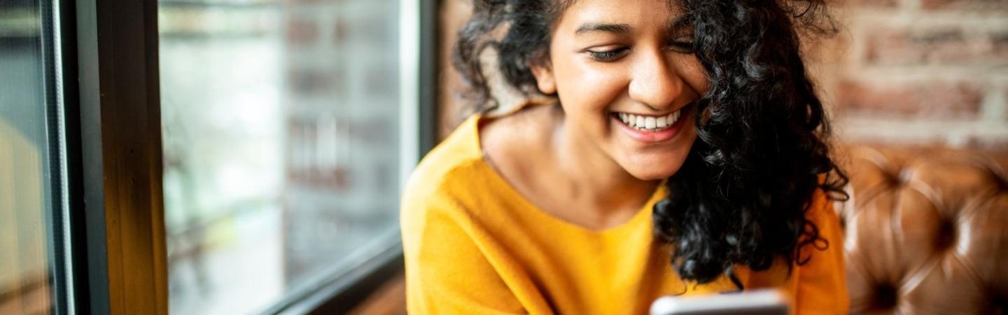 Image shows a woman smiling at her phone. 
